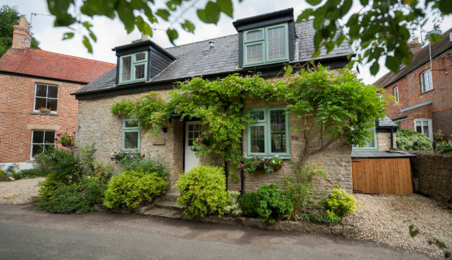 Stone cottage with green flush sash windows and climbing wisteria